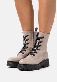 Stivaletti beige in pelle con lacci neri, chiusura con zip e suola in gomma nera texture, dotati di dettagli in cucitura e una asola sul retro.