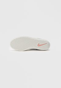 Hvit skosåle med teksturert grep og rosa Nike swoosh-logo på en enkel hvit bakgrunn.