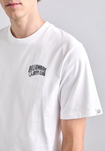 Tricou din bumbac alb cu mâneci scurte, având un print negru cu logo-ul "Billionaire Boys Club" pe pieptul stâng și o etichetă mică pe manșetă.