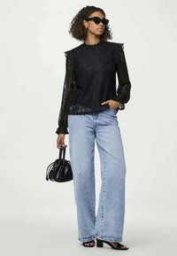 Μαύρη δαντελένια μπλούζα με κοφτό λαιμόκοψη και μακριά διάφανα μανίκια, συνδυασμένη με ανοιχτό μπλε παντελόνι φάρδους και μαύρες στιλέτο σανδάλια. Μικρή μαύρη τσάντα χεριού.