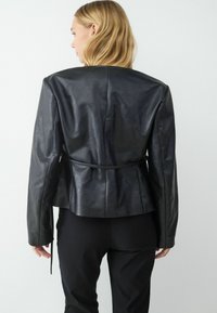 Czarna skórzana kurtka o dopasowanym kroju, z wyraźnymi ramionami i zwężoną talią. Gładka tekstura z delikatnym połyskiem.