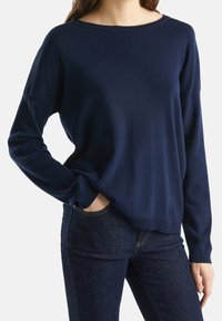 Navyblå stickad tröja med en bred båtärmsringning, långa ärmar, ribbade manschetter och en avslappnad passform, kombinerad med mörka jeans.