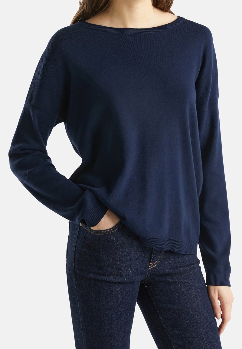 Navyblå stickad tröja med en bred båtärmsringning, långa ärmar, ribbade manschetter och en avslappnad passform, kombinerad med mörka jeans.