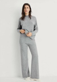 Hellgrauer Strickpullover und passende weit geschnittene Hose, die eine weiche Textur und einen Rundhalsausschnitt aufweist, präsentiert mit aufgerollten Bündchen am Pullover.