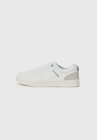 Zapatillas blancas informales con un diseño perforado y acentos en gris claro, con cordones y branding en el lateral, exhibidas sobre un fondo liso.