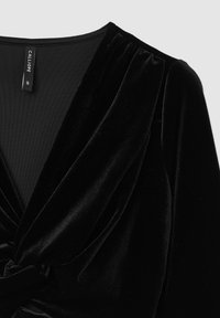 Top in velluto nero con scollatura a V profonda, maniche arricciate e dettaglio a nodo intrecciato sul davanti. Texture morbida e design elegante.