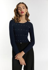 Marineblauer gerippter Pullover mit langen Ärmeln, verziert mit verstreuten Strasssteinen, kombiniert mit schwarzen hochgeschnittenen Hosen.