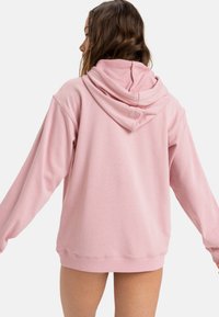 Ružová mikina vyrobená z jemného materiálu, s voľným strihom a kapucňou so sťahovacou šnúrkou. Rukávy sú dlhé a s manžetami, s hladkou textúrou.