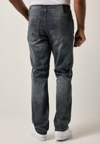 Jeans de mezclilla azul oscuro con corte recto, cinco bolsillos y una textura ligeramente desvaída. Presentan una etiqueta en la cinturilla y zapatillas blancas.