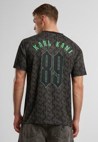 Juoda raštuota trumpomis rankovėmis marškinėliai su "KARL KANI" ir "89" žaliais užrašais nugaroje, laisvas siluetas ir minkšta tekstūra.