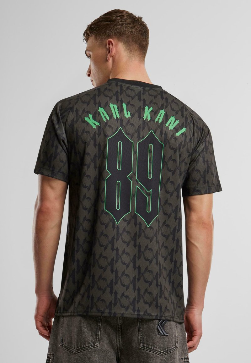Juoda raštuota trumpomis rankovėmis marškinėliai su "KARL KANI" ir "89" žaliais užrašais nugaroje, laisvas siluetas ir minkšta tekstūra.
