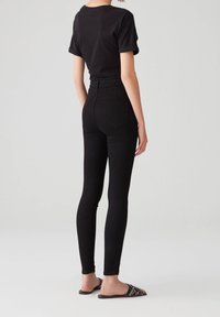 Maglietta nera aderente con maniche arrotolate, abbinata a jeans skinny neri a vita alta. Indossata con sandali neri aperti con dettagli di borchie.