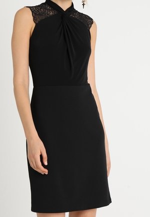 Black sleeveless dress featuring a twisted front design and lace detailing on shoulders. Textured fabric with a fitted silhouette and knee-length hem.