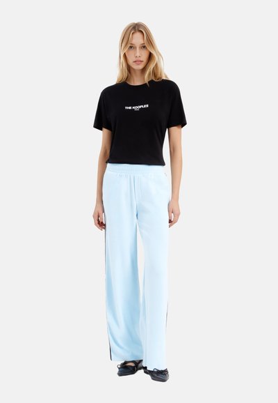 T-shirt nera a maniche corte con testo bianco "THE KOOPLES", abbinata a pantaloni larghi blu chiaro con strisce nere sui lati e cintura elastica.