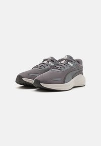 Zapatillas deportivas grises con parte superior de malla transpirable, suela acolchada y suela de goma texturizada. Presenta un logotipo prominente y un sistema de cordones.