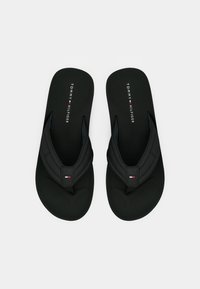 Μαύρα φλιπ-φλοπ με μαξιλαρωμένο πόδι στα δάχτυλα, με λογότυπο στην πατούσα και μικρή επωνυμία στο λουρί. Εξωτερική σόλα από καουτσούκ.