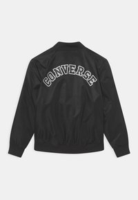 Černá bomber bunda s žebrovanými manžetami a límcem, "CONVERSE" vytištěno velkými bílými písmeny obloukem na zadní straně.