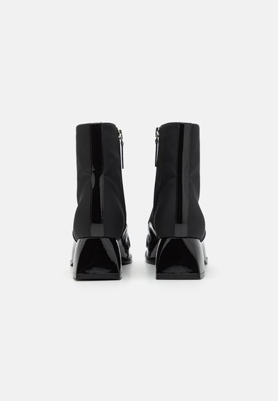 Bottines noires avec un talon en cuir verni brillant et une fermeture éclair, dotées d'un dessus en tissu doux et d'une forme structurée avec un design de talon bloc.