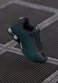 Nike kedas ar melnu un tumši zaļu sietu augšdaļu, teksturētu apdari, unikālu mīksto zoli un melnām šņorēm.