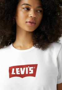 Camiseta de algodón blanca con un destacado logo rojo de Levi's en un diseño clásico en curva. Mangas cortas, cuello redondo, textura suave.
