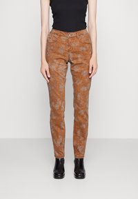 Calças laranja com padrão slim fit, apresentando uma textura de estampa de animal distinta e um design tradicional de cinco bolsos, combinadas com botas pretas.