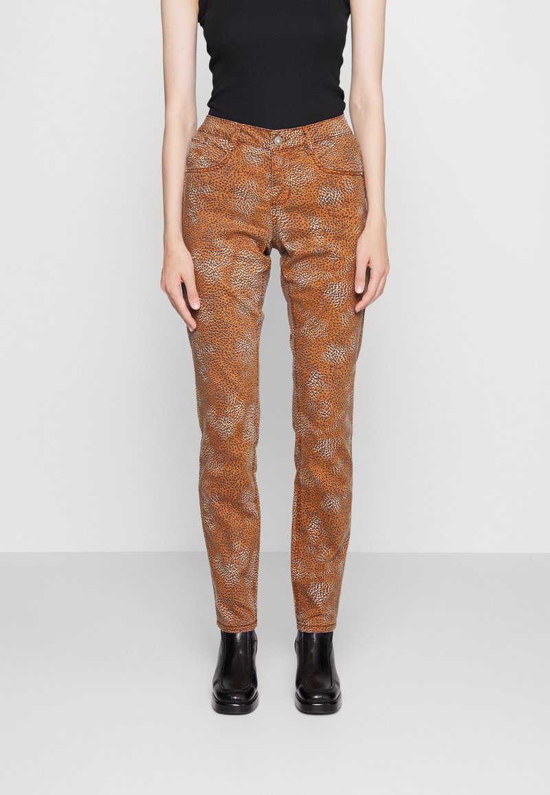 Calças laranja com padrão slim fit, apresentando uma textura de estampa de animal distinta e um design tradicional de cinco bolsos, combinadas com botas pretas.