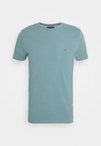 Světle modré tričko s krátkým rukávem a kulatým výstřihem, na levé straně hrudi s malým logem Tommy Hilfiger a pruhovaným detailem uvnitř límce.