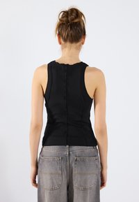 Svart ribbad tanktop med bølgete hals, tettsittende design og synlige sømmer; kombinert med lysegrå høytlivsbukser.