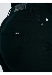 Primer plano de unos vaqueros negros Big Star que muestran el bolsillo trasero, la trabilla del cinturón y las etiquetas con el logo de la marca en la pretina y el bolsillo.