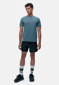 Blå kortermet T-skjorte, sorte shorts, sorte joggesko og hvite sokker med svart mønster. Enkel design og atletisk passform.