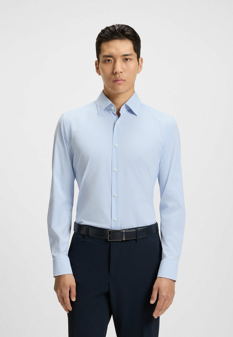 Ljusblå randig skjorta i slät tyg, med knapp-down krage och långa ärmar, kombinerad med mörka byxor.