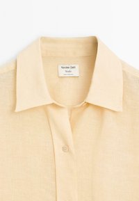 Beige Leinenhemd mit Button-Down-Kragen und durchgehender Knopfleiste. Der Stoff hat eine strukturierte Oberfläche und ist innen am Kragen mit einem Markenlabel versehen.