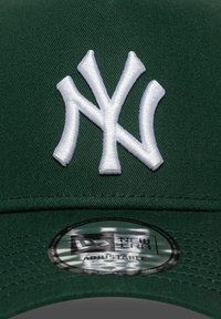 Grüne Baseballmütze mit einem erhabenen, weißen gestickten "NY"-Logo, flexibrem Schirm und einem runden Etikett mit der Aufschrift "New Era Adjustable."