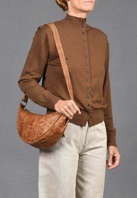 Cárdigan marrón con cierre de botones, combinado con un bolso marrón texturizado y curvado que cuenta con una correa para el hombro y herrajes metálicos.