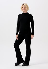 Haut noir à manches longues avec col montant, associé à un pantalon noir ajusté à bas évasé. Texture lisse, matériau extensible, adapté à la maternité.