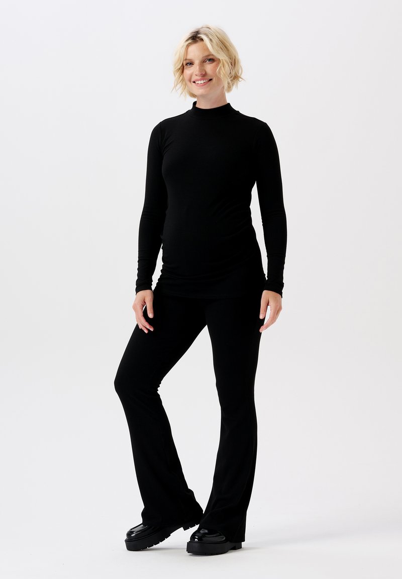 Haut noir à manches longues avec col montant, associé à un pantalon noir ajusté à bas évasé. Texture lisse, matériau extensible, adapté à la maternité.