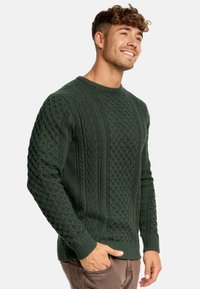 Ciemnozielony sweter wykonany w splot kablowy z fakturowanymi wzorami, z prążkowanymi mankietami i dołem. Design z okrągłym dekoltem, wykonany z miękkiego materiału.