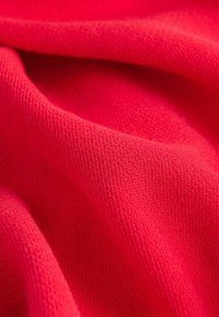 Červená látka s měkkým, texturovaným pletením. Materiál je hladký a mírně elastický, s jemnými detaily tkaní viditelnými po celém povrchu.