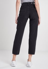 Vaqueros de mezclilla negros con cintura alta y corte recto. Con dos bolsillos traseros y una textura suave. Combinados con zapatillas blancas.