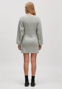 Robe-pull grise avec des manches raglan longues, un col rond et une silhouette ajustée. Texture douce, détails de couture minimaux.