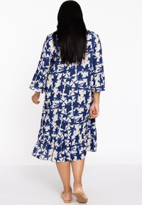 Weißes und blaues blumengemustertes Kleid mit schwingendem Saum, dreiviertel Ärmeln und lässiger Passform. Hergestellt aus leichtem Stoff.