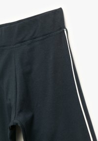 Donkere marineblauwe leggings met een zachte textuur, voorzien van een brede tailleband en een witte zijsstrik voor contrast.