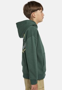 Grüne Kapuzenjacke mit Kängurutasche, gerippten Bündchen und gelben Logodetails an der Seite. Weicher, strukturierten Stoff.