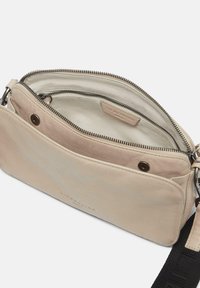 Beige Leder Umhängetasche mit einem Reißverschlussfach, glatter Textur und abnehmbarem Tragegurt. Mit Logodetails auf der Vorderseite.