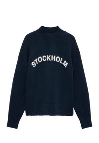 Mornarsko modra pletena jopica z širokim telesom, rebrastim ovratnikom in besedo "STOCKHOLM" v beli barvi, ki se lomi čez prsa.
