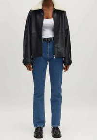 Chaqueta de cuero negra con un collar de piel sintética crema, combinada con jeans de mezclilla azul de cintura alta y zapatos negros con cordones.