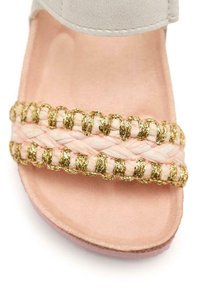 Infradito rosa chiaro con una fascia intrecciata e dettagli dorati. Texture morbida con suola piatta, progettate per un uso casual.
