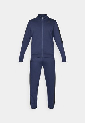 Survêtement bleu marine avec un design ajusté. La veste zippée présente un col montant et des rayures latérales noires ; le pantalon assorti dispose de poignets élastiques.