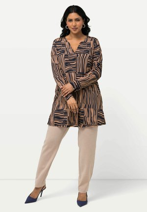 Tunique longue beige avec des rayures marines, associée à un pantalon beige ajusté et des talons hauts bleus, avec un décolleté en V et des manches longues.