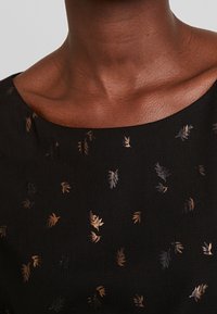 Tissu noir avec un motif de feuilles éparpillées subtile en tons de bronze et d'or ; texture lisse avec un décolleté large et arrondi.